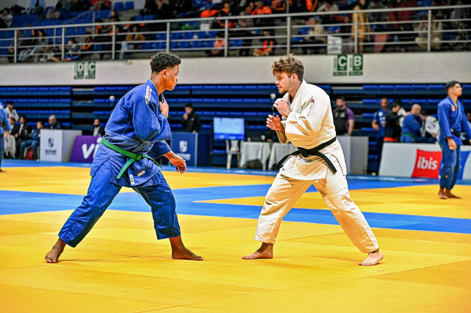 Dois judocas em guarda, frente a frente no tatame durante campeonato